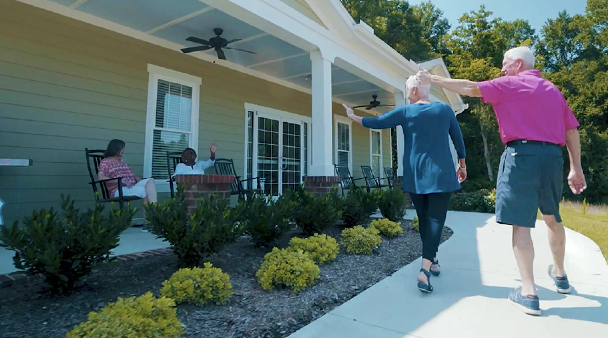 A couple approaches a retirement center and waves to residents relaxing on the porch in North Carolina